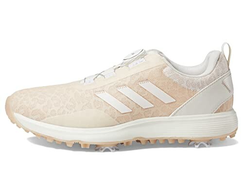 Beige Adidas golf shoe with white stripes and textured design.