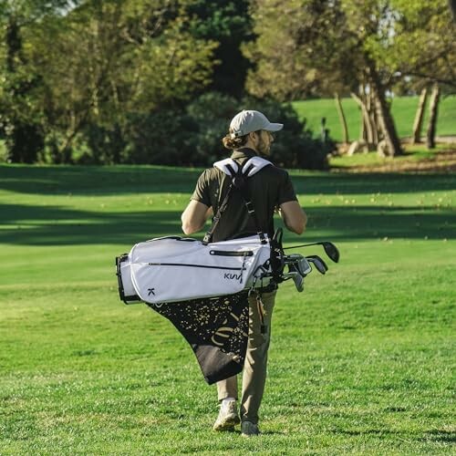 Golfer carrying a golf bag on a green course.